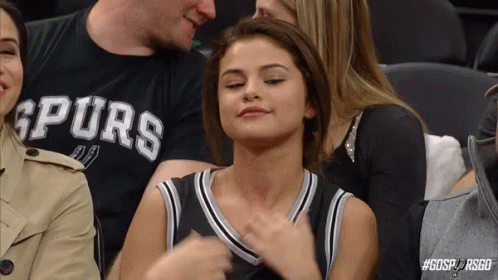 A Woman Is Sitting In The Stands At A Basketball Game Wearing A Spurs Shirt . GIF