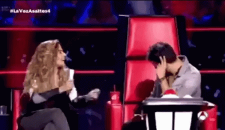 A Woman Is Sitting Next To A Man In A Red Chair Covering His Face With His Hand . GIF