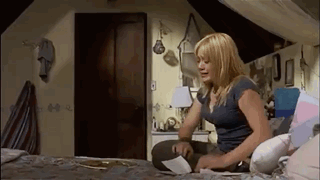 a woman is sitting on a bed in an attic room looking at a piece of paper .