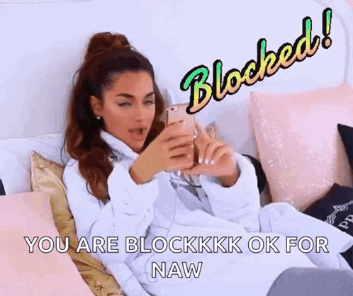 A Woman Is Sitting On A Bed Looking At Her Phone With The Words `` You Are Blockkkk Ok For Naw '' Above Her . GIF