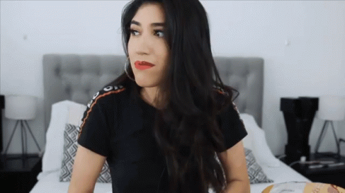 A Woman Is Sitting On A Bed With A Bag Of Doritos GIF