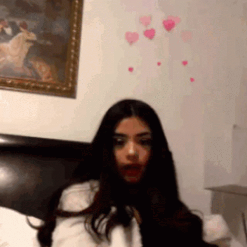 A Woman Is Sitting On A Bed With A Picture Of A Horse On The Wall Behind Her GIF