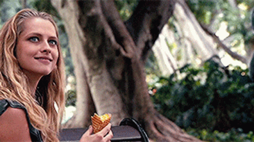A Woman Is Sitting On A Bench Holding An Ice Cream Cone And Smiling . GIF