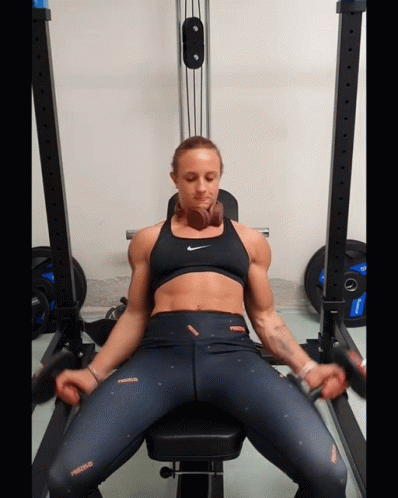 a woman is sitting on a bench in a gym wearing a nike top