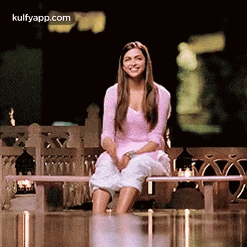 A Woman Is Sitting On A Bench With Her Legs Crossed And Smiling At The Camera . GIF