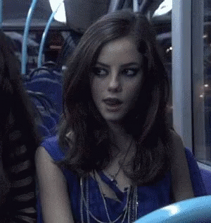 A Woman Is Sitting On A Bus Wearing A Blue Top And Necklaces . GIF