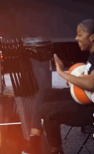 A Woman Is Sitting On A Chair Holding A Basketball And Giving A High Five . GIF