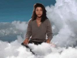 A Woman Is Sitting On A Cloud With A Blue Sky Behind Her GIF