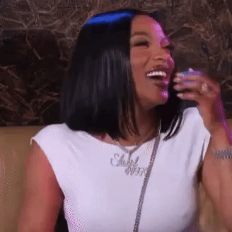 A Woman Is Sitting On A Couch And Laughing While Wearing A White Shirt . GIF