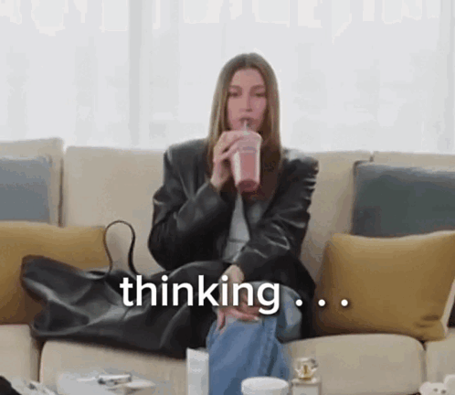 A Woman Is Sitting On A Couch Drinking A Smoothie And The Word Thinking Is On The Screen GIF