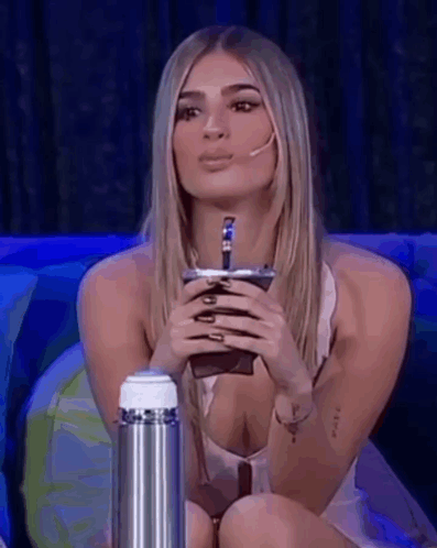 A Woman Is Sitting On A Couch Holding A Cup In Her Hand . GIF