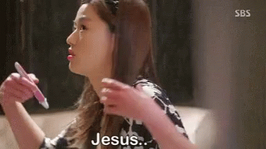 A Woman Is Sitting On A Couch Holding A Pen In Her Hand And Saying Jesus . GIF