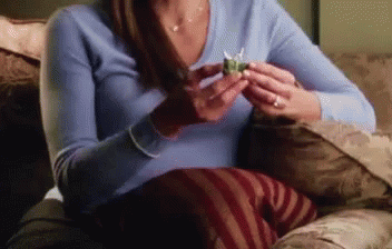 A Woman Is Sitting On A Couch Holding A Small Object In Her Hand . GIF