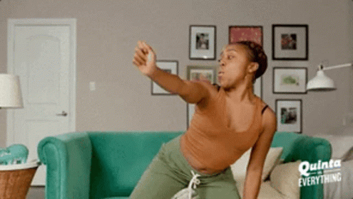 A Woman Is Sitting On A Couch In A Living Room With A Sign That Says Everything GIF
