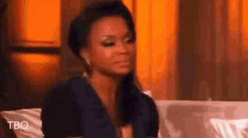 A Woman Is Sitting On A Couch Making A Funny Face And Looking At The Camera . GIF