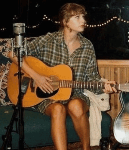 A Woman Is Sitting On A Couch Playing A Guitar . GIF