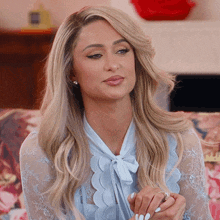 A Woman Is Sitting On A Couch Wearing A Blue Lace Shirt And A Bow Tie . GIF