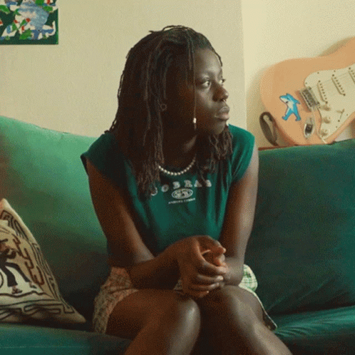 A Woman Is Sitting On A Couch Wearing A Green Shirt That Says Jobea On It GIF