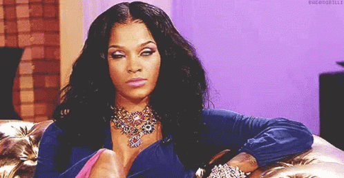 A Woman Is Sitting On A Couch Wearing A Necklace And Bracelets And Making A Funny Face . GIF