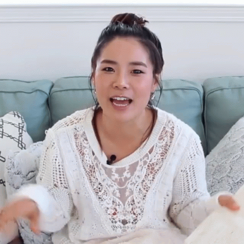 A Woman Is Sitting On A Couch Wearing A White Sweater GIF
