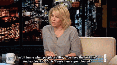 A Woman Is Sitting On A Couch With A Cup That Says A Late Show On It GIF