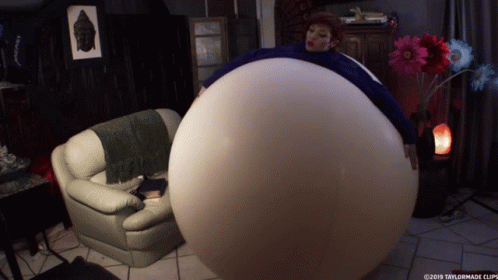 A Woman Is Sitting On A Couch With A Large Balloon Around Her Belly GIF