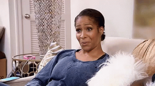 A Woman Is Sitting On A Couch With A White Pillow And A Cell Phone . GIF