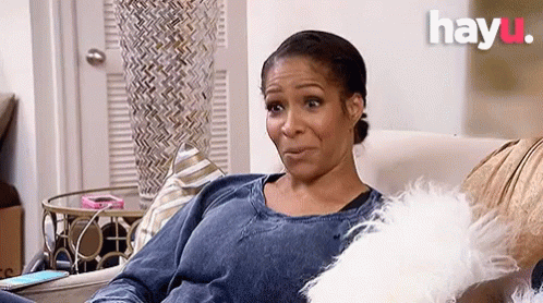 A Woman Is Sitting On A Couch With A White Pillow And A Phone . GIF