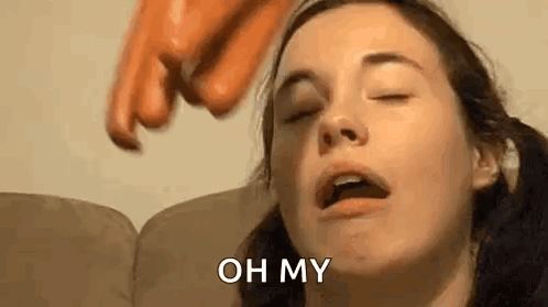 A Woman Is Sitting On A Couch With Her Eyes Closed While A Sausage Is Being Thrown At Her Head . GIF