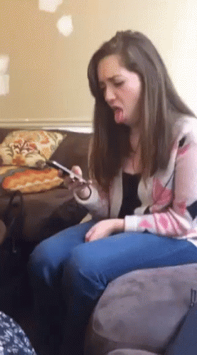 A Woman Is Sitting On A Couch With Her Tongue Out And Looking At Her Phone GIF