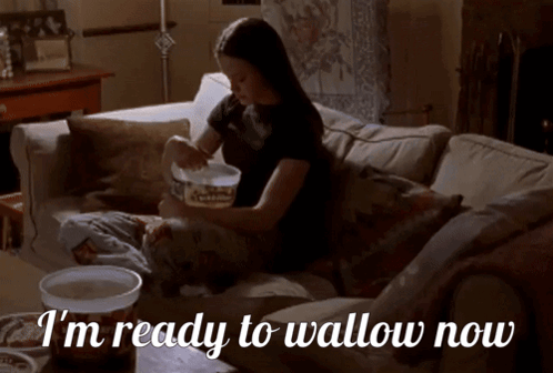 A Woman Is Sitting On A Couch With The Words I 'M Ready To Wallow Now GIF