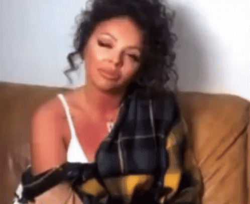 A Woman Is Sitting On A Couch Wrapped In A Blanket And Holding A Scarf . GIF