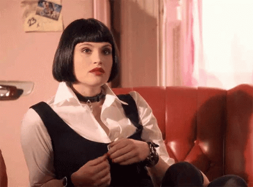 A Woman Is Sitting On A Red Couch Wearing A Choker And A Wig . GIF