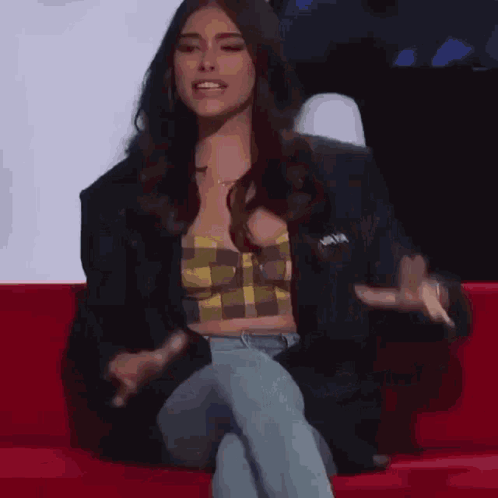 A Woman Is Sitting On A Red Couch With Her Legs Crossed And Talking . GIF