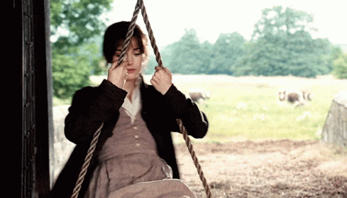A Woman Is Sitting On A Rope Swing In A Field With Sheep In The Background GIF