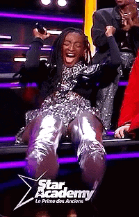 A Woman Is Sitting On A Stage In A Star Academy Le Prime Des Anciens Show And Laughing . GIF