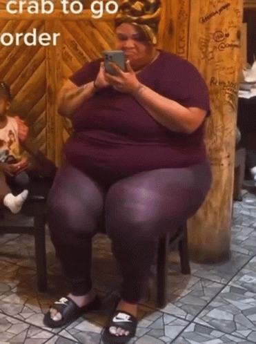 A Woman Is Sitting On A Stool Looking At Her Phone With The Words " Crab To Go Order " Written Above Her GIF