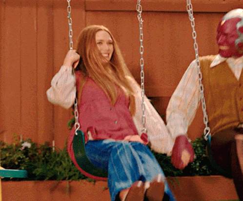 A Woman Is Sitting On A Swing Next To A Man In A Mask GIF