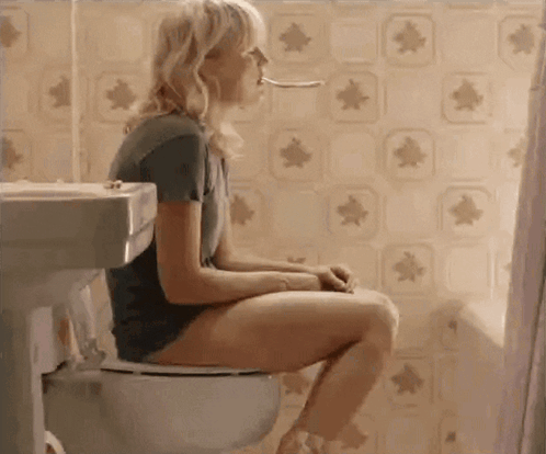 A Woman Is Sitting On A Toilet In A Bathroom With A Spoon In Her Mouth GIF