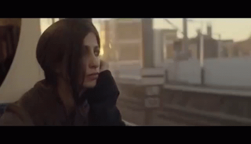 A Woman Is Sitting On A Train Looking Out The Window At The City . GIF