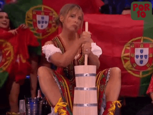 A Woman Is Sitting On A Wooden Barrel With A Flag In The Background GIF