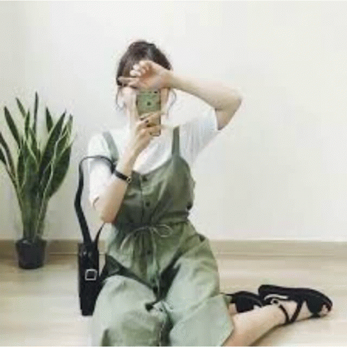 A Woman Is Sitting On The Floor Taking A Selfie With Her Cell Phone . GIF