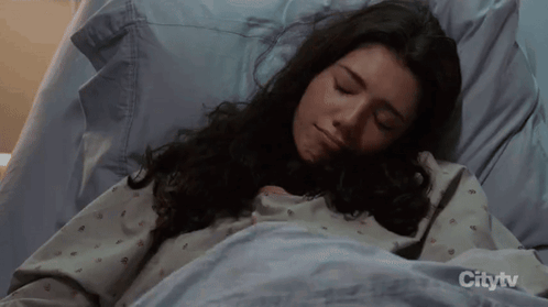 A Woman Is Sleeping In A Hospital Bed With Citytv On The Bottom GIF