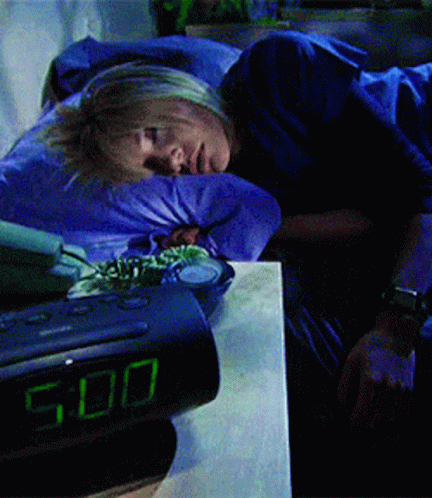 A Woman Is Sleeping Next To An Alarm Clock That Shows The Time As 5:00 GIF