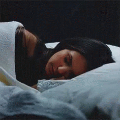 A Woman Is Sleeping On A Bed With A White Blanket GIF