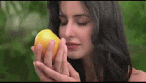 A Woman Is Smelling A Lemon In Her Hand . GIF