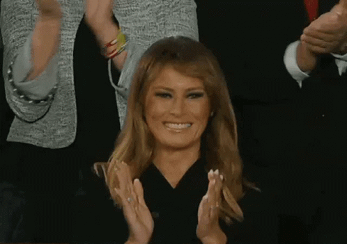 A Woman Is Smiling And Clapping Her Hands In Front Of A Crowd Of People . GIF