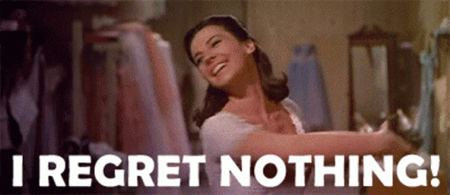 A Woman Is Smiling And Dancing In A Room With The Words `` I Regret Nothing '' Written On The Bottom . GIF