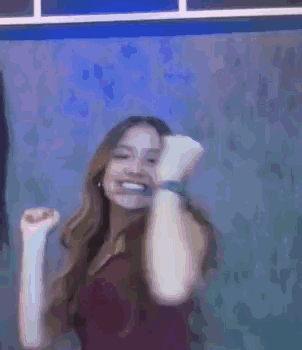 A Woman Is Smiling And Dancing In Front Of A Blue Wall . GIF