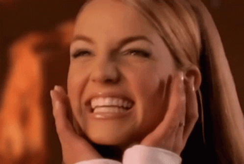 A Woman Is Smiling And Holding Her Face With Her Hands . GIF